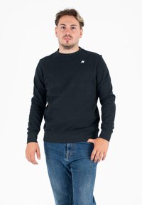 Ciemnogranatowy sweatshirt wykonany z miękkiego materiału, z okrągłym dekoltem, prążkowanymi mankietami oraz małym logo na piersi. Noszony z niebieskimi dżinsami.