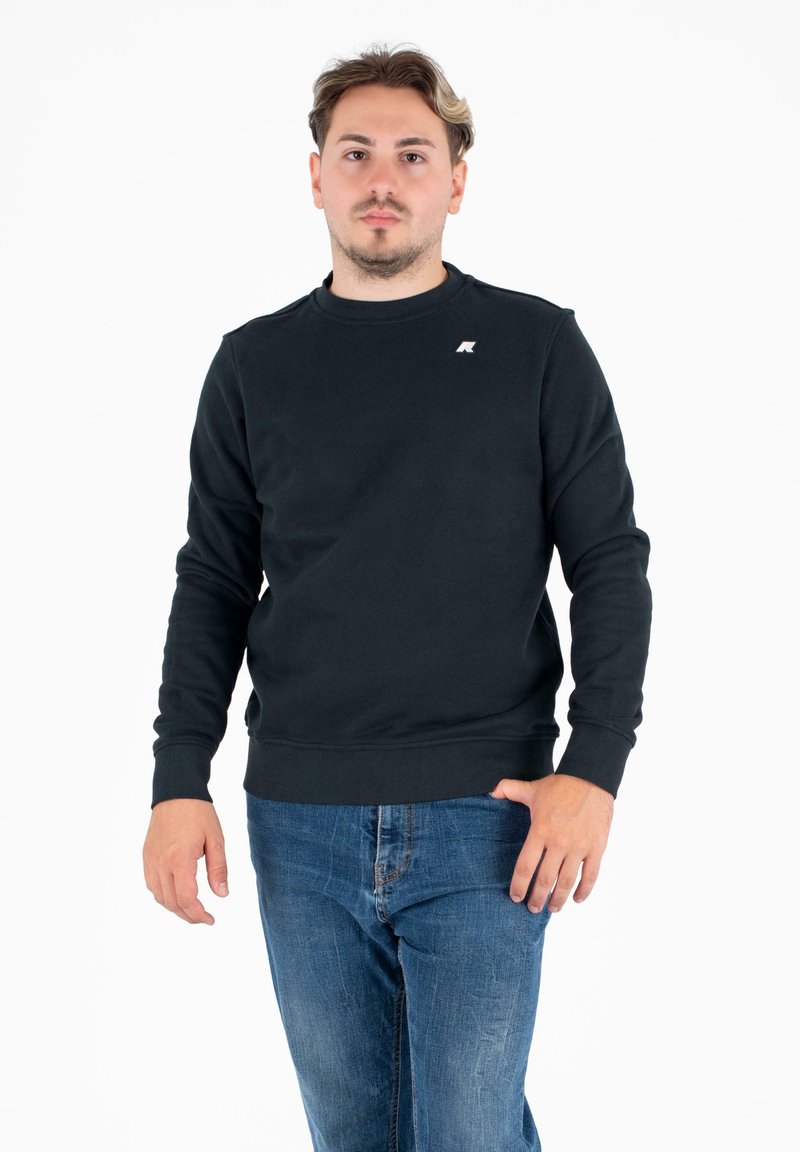 Ciemnogranatowy sweatshirt wykonany z miękkiego materiału, z okrągłym dekoltem, prążkowanymi mankietami oraz małym logo na piersi. Noszony z niebieskimi dżinsami.