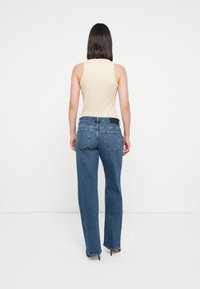 Beige ermeløs tanktopp kombinert med blå rette jeans. Jeansene har mørk liv med to baklommer. Glatt tekstur.