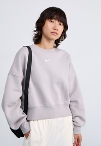 Ljusgrå sweatshirt med ribbat rundhals, ballongärmar, elastisk nederdel och en liten vit Nike-logga på bröstet.