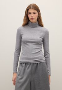 Grauer, gerippter Rollkragenpullover mit langen Ärmeln. Glatte Struktur und figurbetontes Design, kombiniert mit lockeren grauen Hosen.