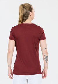 Bordeaux kortærmet t-shirt med rund halsudskæring, glat tekstur og tætsiddende design. Har minimal dekoration og sidesømme.