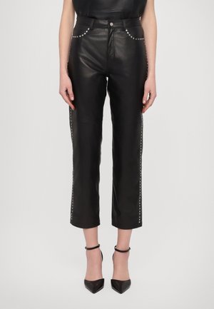 Schwarze, gekürzte Lederhose mit silbernen Nieten entlang der Taschen und der Seitennähte, getragen mit schwarzen spitzen Pumps mit Knöchelriemen.