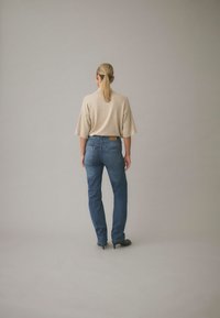 Beige oversized topp kombinerad med mörkblå jeans. Jeansen har en klassisk passform med bakfickor och en läderetikett på midjebandet.
