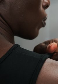 Κοντινό ενός ατόμου με σκούρο δέρμα που φοράει μαύρο τοπ, δείχνοντας τον λαιμό, τον ώμο και το χέρι που ακουμπά στον ώμο.