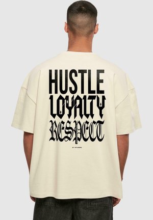 Krémové bavlnené oversized tričko s veľkým čiernym textom na chrbte: "HUSTLE LOYALTY RESPECT." Krátke rukávy a uvoľnený strih.