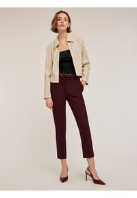 Beige perforerad läderjacka, svart ribbad topp, vinröda avsmalnande byxor och vinröda spetsiga klackar, vilket skapar en stilren outfit.