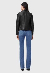 Zwarte leren jas met een slim fit ontwerp, brede kraag en schuine ritsen, gecombineerd met blauwe high-waisted jeans en zwarte hakken.