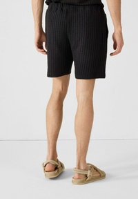 Pantalones cortos negros texturizados con un diseño de malla, que cuentan con una cintura elástica y bolsillos laterales, combinados con sandalias casuales beige.