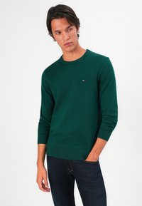 Pulover verde tricotat pentru bărbați, cu mâneci lungi, guler rotund și un mic accent cu logo pe piept. Material texturat cu manșete cu nervuri.