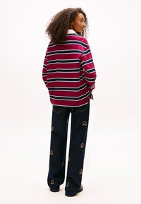 Pasiasty bordowo-granatowy sweter z białymi akcentami, zestawiony z ciemnymi dżinsami ozdobionymi kolorowym haftem koron.