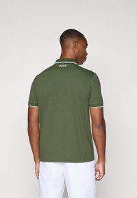 Polo verde con dettagli bianchi, progettato con colletto e maniche corte. Presenta il nome del marchio "BOSS" nella zona del collo sul retro.