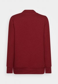Sweatshirt matelassé bordeaux avec un col arrondi, des manches longues, et des bords côtelés au niveau des poignets et de l'ourlet. Texture lisse avec un motif en losange.