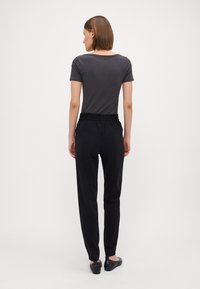 Pantalons noirs à taille élastique avec une coupe décontractée, associés à un t-shirt gris ajusté, présentés de dos. Tissu lisse, design simple.