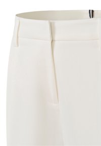 Gros plan sur la ceinture d'un pantalon blanc avec passants pour ceinture et fermeture éclair avant cachée.