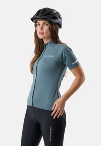 Femme portant un casque de vélo noir, un maillot de cyclisme à manches courtes bleu clair et un short de cyclisme noir avec le logo Swedemount sur les deux.