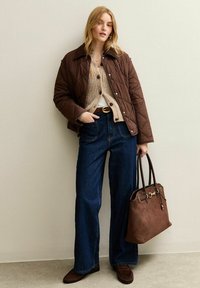 Veste matelassée marron sur un pull en maille beige, jeans larges bleus, sac à main marron foncé et chaussures assorties. Simples accents métalliques sur le sac.