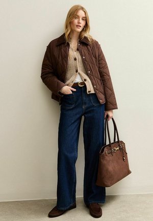 Veste matelassée marron sur un pull en maille beige, jeans larges bleus, sac à main marron foncé et chaussures assorties. Simples accents métalliques sur le sac.