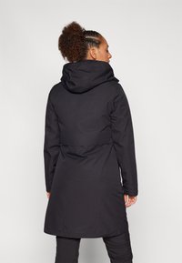 Sort vandtæt parka med hætte, der har en indsnævret talje, lange ærmer og en glat tekstur. Bagfra ses et minimalistisk design.