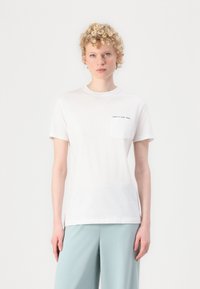 White cotton t-shirt with a round neckline, short sleeves, and a chest pocket featuring black text. Smooth texture, simple design.