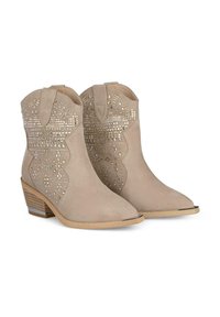 Stivaletti alla caviglia in suede beige con punta appuntita, fori decorativi e borchie metalliche, montati su un tacco basso impilato.