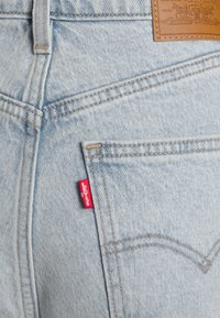 Poche arrière d'un jean en denim bleu clair avec l'étiquette rouge signature de Levi's et un patch en cuir marron montrant le logo de la marque et les détails des coutures.