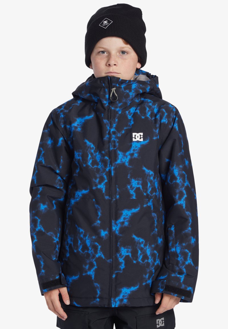 Svart och blå mönstrad vinterjacka med huva, med en DC-logotyp på bröstet och kardborrestängning på ärmarna. Tyget ser strukturerat ut.