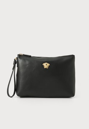 Bolso de mano de piel negra con un emblema de Medusa dorado, cierre de cremallera y correa desmontable, con una textura suave y forma rectangular.