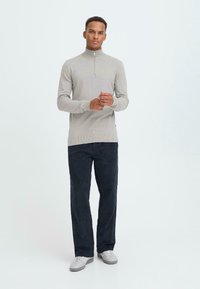 Lys grå strikket genser med halvdempet glidelås og ribbede mansjetter, kombinert med mørk marineblå kordfløyelsbukser og grå joggesko. Enkelt og funksjonelt design.