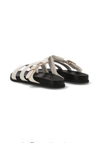 Sandalias blancas de tiras con suelas planas negras y hebillas laterales ajustables, mostradas desde la parte trasera sobre un fondo blanco.