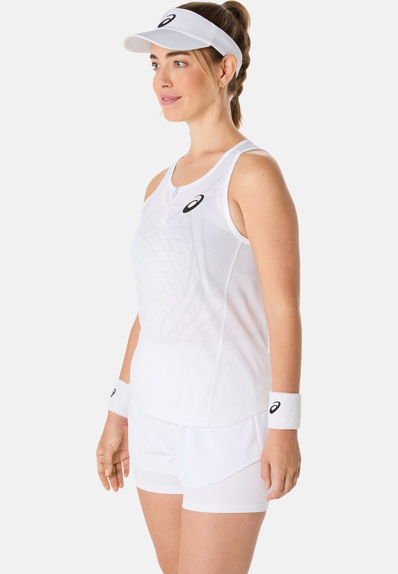 Camiseta de deporte blanca sin mangas con paneles de malla, cuello con cremallera, combinada con pantalones cortos blancos. Muñequera blanca y visera con acentos de logotipo negros.