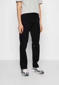 Black trousers with a straight cut, made from durable fabric. Features a waistband with belt loops and a small logo detail near the hem.