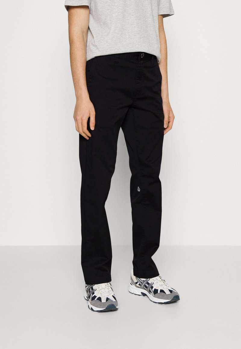 Black trousers with a straight cut, made from durable fabric. Features a waistband with belt loops and a small logo detail near the hem.