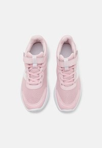 Chaussures de sport roses avec une tige en maille, des accents blancs, un embout renforcé et une sangle Velcro pour un maintien sécurisé. Design classique à lacets.