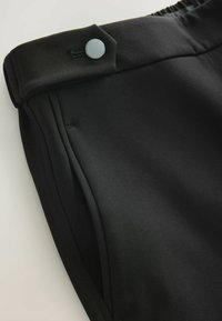 Černé kalhoty z hladkého materiálu, s uzavíráním na knoflík, elastickým pasem a bočními kapsami. Jednoduchý design a přizpůsobený tvar.
