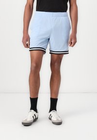 Shorts de sport en maille bleu clair avec une taille élastique noire et des rayures sur les côtés. Associés à des chaussettes noires et des baskets blanches.