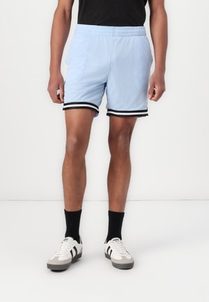 Lichtblauwe mesh sportshorts met een zwarte elastische tailleband en zijkanten. Gecombineerd met zwarte sokken en witte sneakers.