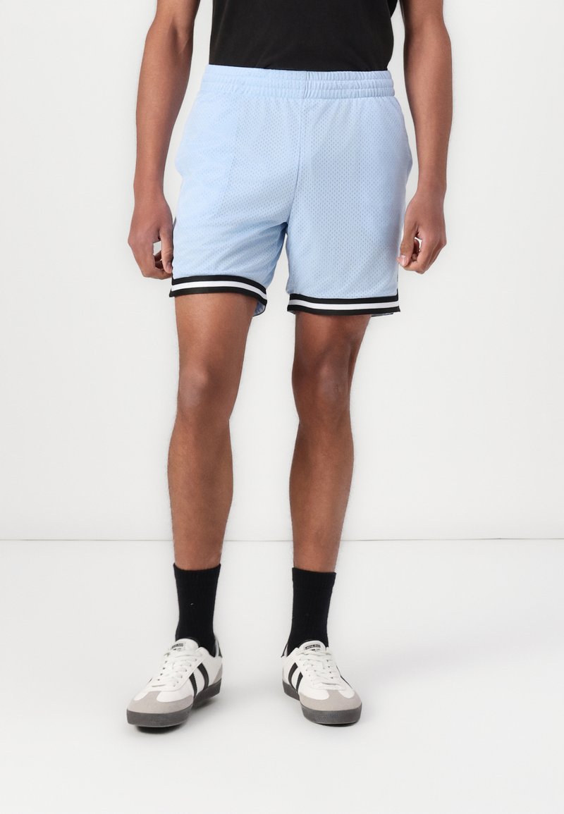 Shorts de sport en maille bleu clair avec une taille élastique noire et des rayures sur les côtés. Associés à des chaussettes noires et des baskets blanches.
