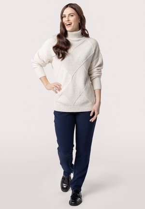 Cream turtleneck sweater with diagonal textured patterns, paired with navy pants and black shoes. Soft, knitted material and relaxed fit.