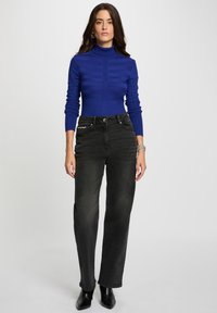 Maglione a collo alto a coste blu reale con strisce orizzontali abbinato a jeans neri a vita alta a gamba dritta e stivali alla caviglia.