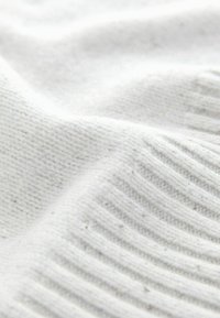 White knitted fabric featuring a soft texture with a combination of smooth and ribbed patterns. Subtle flecks are visible throughout.