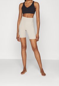 Shorts da bicicletta beige a vita alta realizzati in tessuto elastico, con una texture liscia e lunghezza fino a metà coscia, abbinati a un reggiseno sportivo nero a scollo a V.