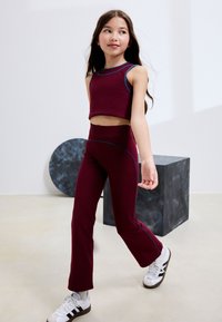 Top corto color marrone scuro e pantaloni a vita alta svasati abbinati con accenti blu. L'outfit presenta una texture liscia e un design aderente.