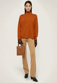 Spalony pomarańczowy sweter z golfem, beżowe rozszerzane spodnie, ciemnobrązowe rękawiczki oraz mała brązowa skórzana torebka z logo. Czarne botki na obcasie.