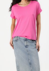 Fuksjowy T-shirt z krótkim rękawem i podwiniętymi mankietami, połączony z jasnoniebieską spódnicą dżinsową. Materiał wydaje się miękki i gładki.