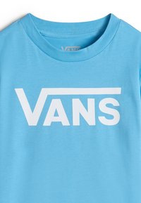 Světle modré tričko vyrobené z bavlny s velkým bílým logem "VANS" v tučném písmu na přední straně. Kulatý výstřih, krátké rukávy.