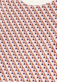 Primer plano de tela con un patrón geométrico repetido de triángulos marrones y pequeñas formas negras similares a estrellas sobre un fondo rosa claro.