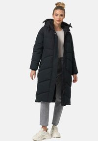 Black puffer coat with hood, zippered front, quilted design, long sleeves, and two side pockets, paired with gray jeans and white sneakers.