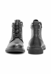 Para czarnych skórzanych botków do kostki, jeden pokazujący przód z sznurowadłami, a drugi pokazujący tył z pętelką do zakładania i bocznym zamkiem.