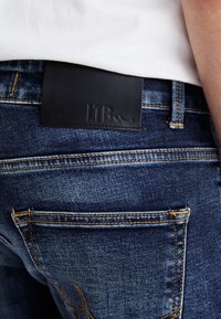 Blue denim jeans with a dark leather LTB label at the waistband, featuring contrast orange stitching and classic pocket design.